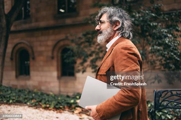 mature professional carrying laptop outdoors near historic building - professor da faculdade imagens e fotografias de stock