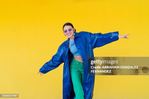 stylish woman posing in blue coat, dark sunglasses against bright yellow backdrop, radiating contemporary urban confidence - fundo colorido imagens e fotografias de stock