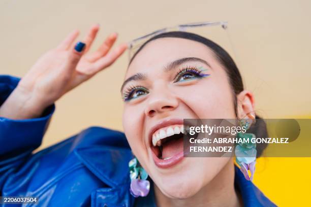 vibrant woman with colorful makeup, laughing heartily, raising hand and radiating pure joy during studio photoshoot - eyeliner stock pictures, royalty-free photos & images