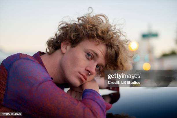 curly-haired person leans on a reflective surface, gazing contemplatively in urban setting. miami, fl, usa - transgender foto e immagini stock