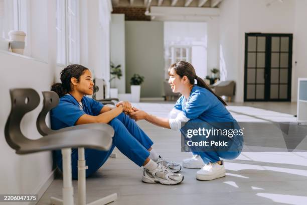female colleague consoling young nurse at hospital corridor - tired healthcare worker stock pictures, royalty-free photos & images