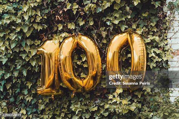 golden balloons forming the number "100" on ivy background, celebrating a 100th birthday. - 100th anniversary stock pictures, royalty-free photos & images