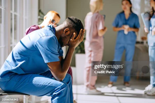 worried male doctor sitting on a chair in wait room of hospital - tired healthcare worker stock pictures, royalty-free photos & images