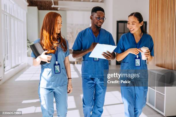 junge kollegen aus dem gesundheitswesen gehen und sprechen auf dem krankenhausflur - krankenpflegepersonal stock-fotos und bilder