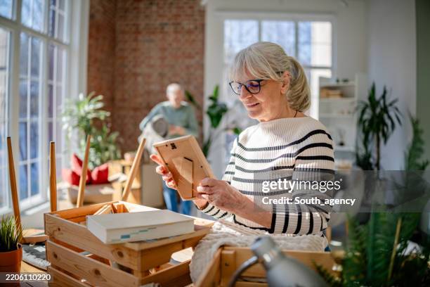 senior couple joyfully decorating their new home together in a bright living room space - uitpakken activiteit stockfoto's en -beelden