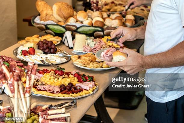 man serving table food of cold cuts, cheeses, fruits, and breads. buffet breakfast. lunch. all you can eat. eat as much as you like restaurant. free fork. - buffet stockfoto's en -beelden