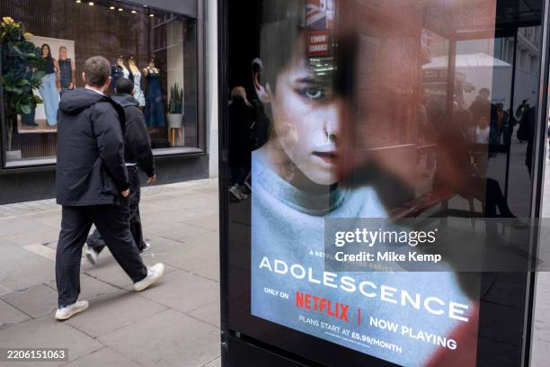 Passing people interacting with an advertising poster on a bus shelter for the Netflix drama 'Adolescence', the story of which is sparking...