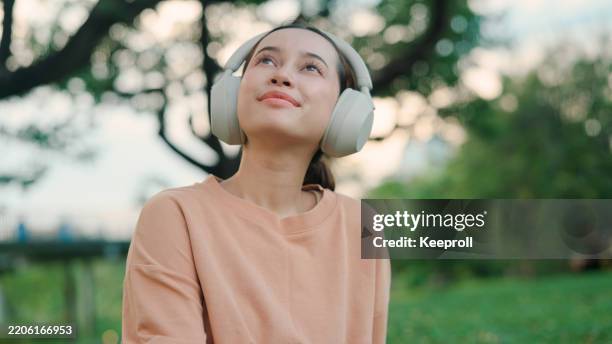 asian young woman listening to music in public park - music therapy stock pictures, royalty-free photos & images