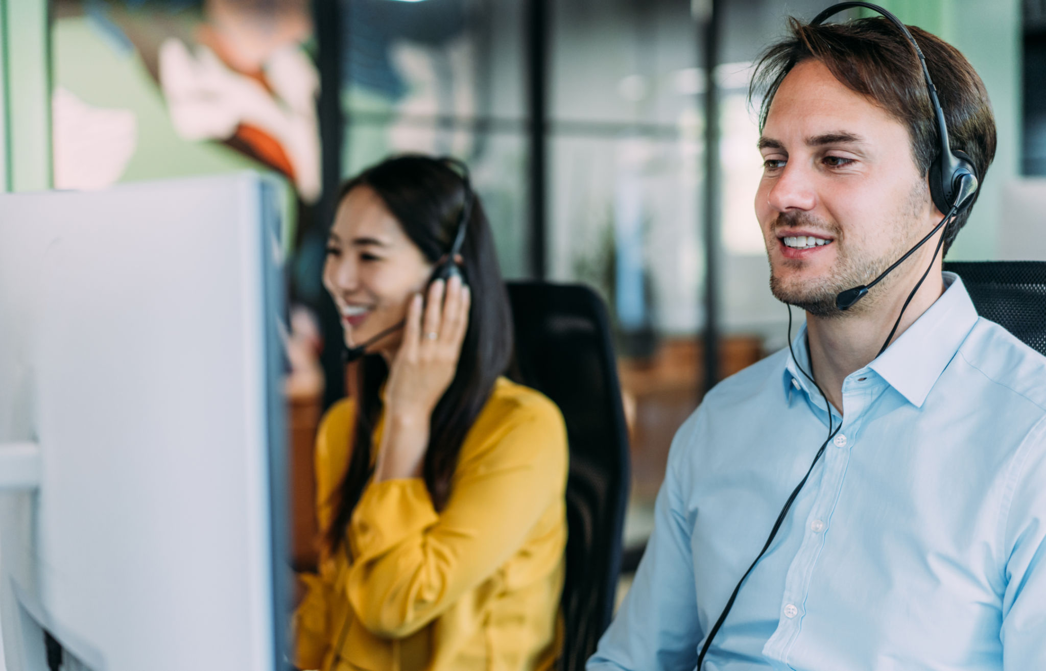 Shot of call center operators working in the office. Call center agent working with his female colleague in modern office. Smiling handsome businessman working in call center.
