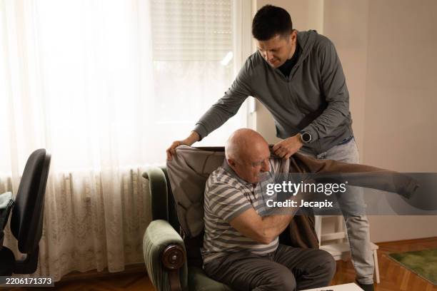 son taking care of his father at home - aankleden stockfoto's en -beelden