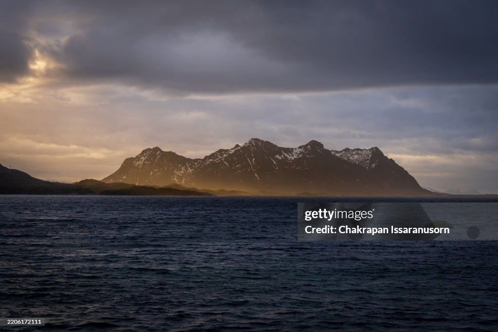 Cordilheira em mar aberto distante com raios de luz durante o nascer do sol em Svolvær, Noruega