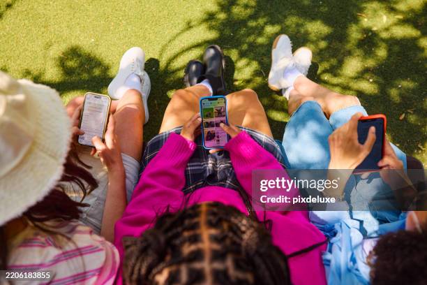 des amis utilisant des smartphones assis sur un banc dans un parc - générique photos et images de collection