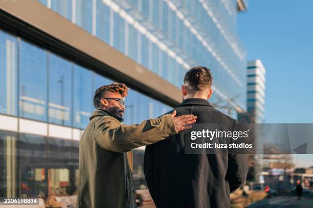 two men walking in urban setting with modern architecture and winter coats - pat on the back stockfoto's en -beelden