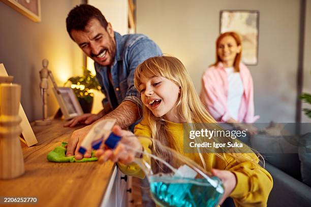famiglia che pulisce casa insieme, figlia che spruzza disinfettante sui mobili - attrezzi per le pulizie foto e immagini stock