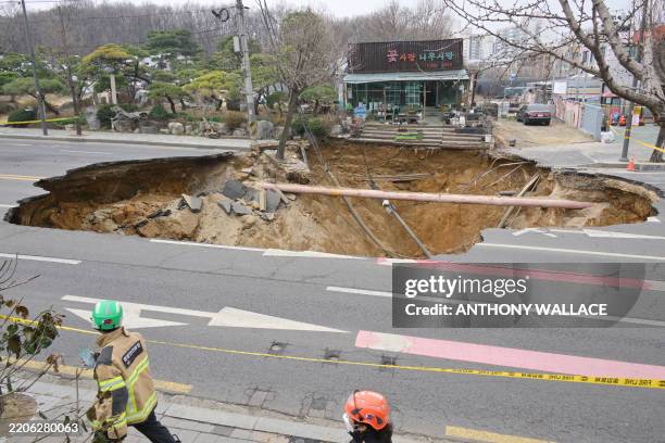 Rescue workers walk past a sinkhole outside a plant shop on a road in Seoul on March 25, 2025. One person has been killed after a massive sinkhole...
