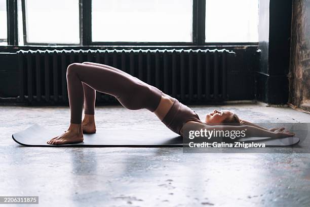 young slim woman in sportswear doing stretching on mat in modern loft studio - estera fotografías e imágenes de stock