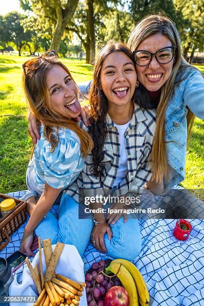 three young women sticking out tongues at picnic in park - cultura argentina imagens e fotografias de stock
