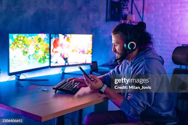 man using mobile phone while playing games in room with neon lighting - componente elétrico imagens e fotografias de stock