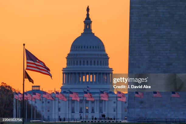 Sunrise turns the sky orange behind the U.S. Capitol building as it illuminates the U.S. Flags circling the base of the Washington Monument on March...