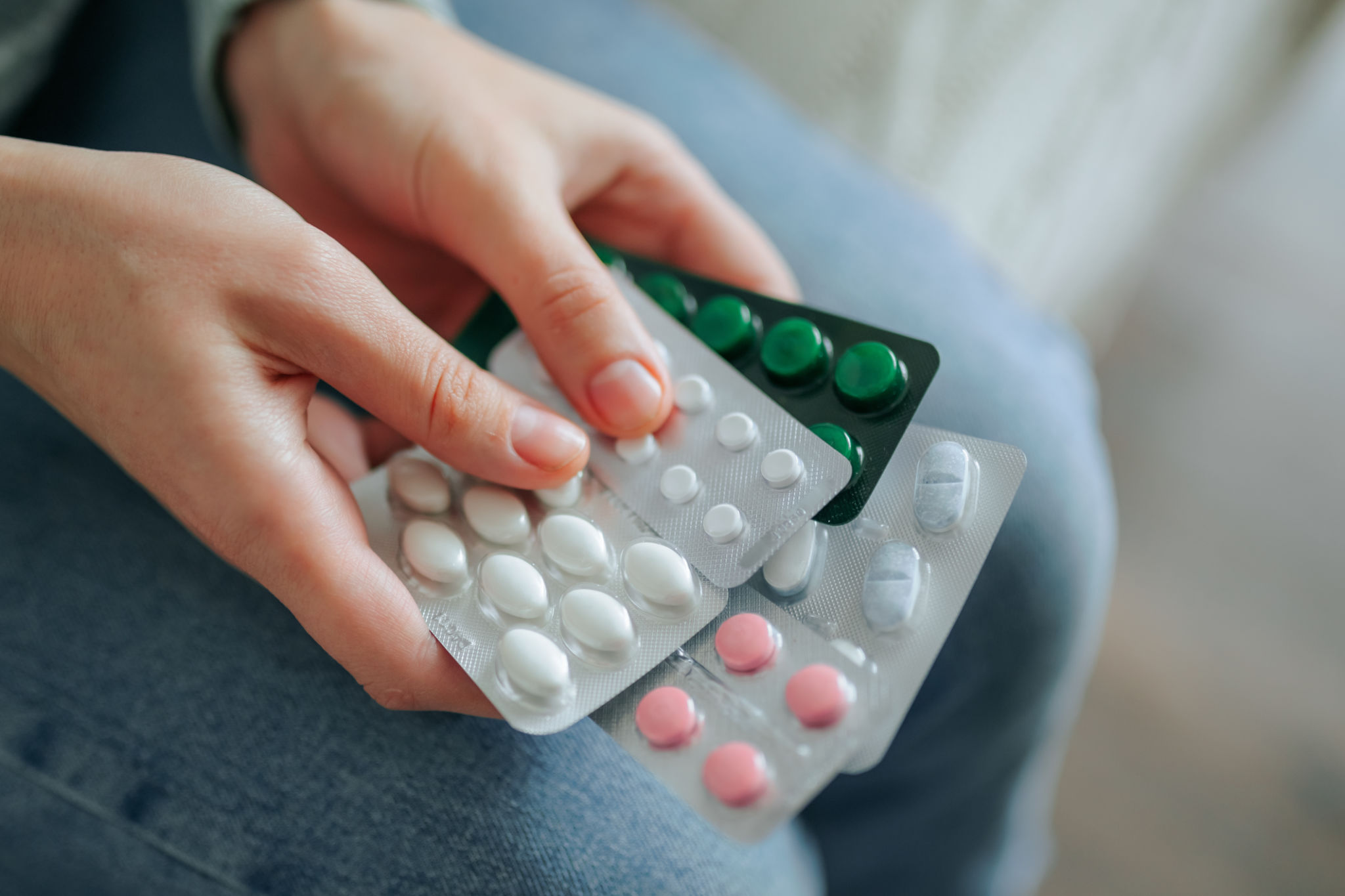Hands holding multiple blister packs of medication in a casual setting Hands holding multiple blister packs of medication in a casual setting
