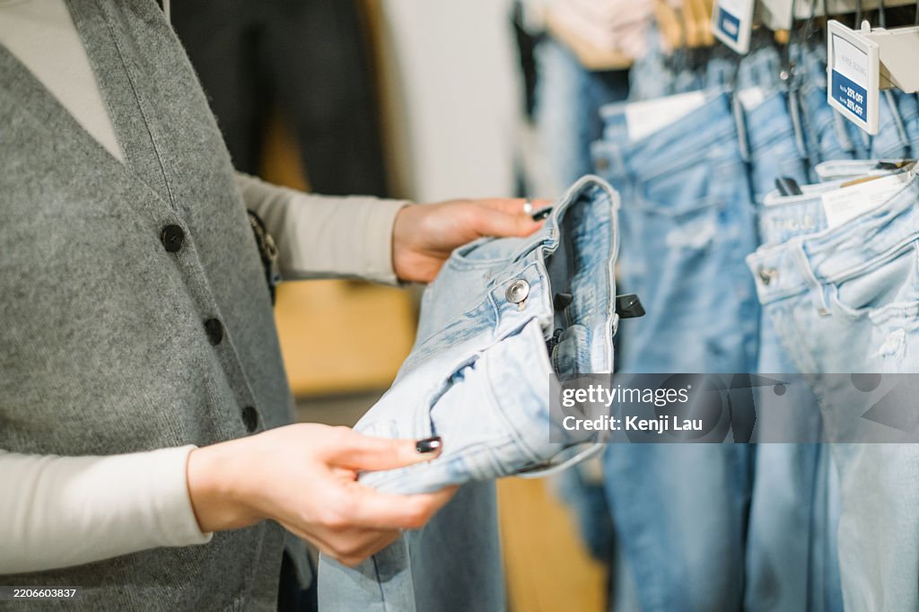 Cropped shot of woman's hand selecting a pair of trousers while shopping in a clothing store in the city.