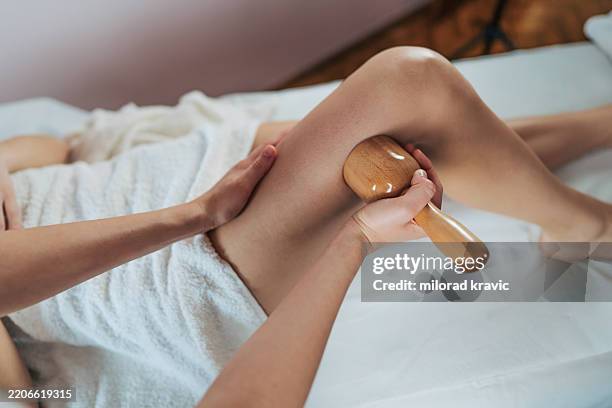 masseuse using wooden maderotherapy tool for leg massage - bloedcirculatie stockfoto's en -beelden