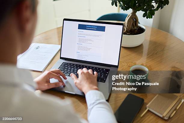 man browsing job listing on laptop at home - über die schulter stock-fotos und bilder