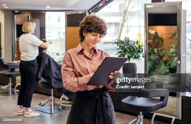 professional hair salon owner with curly hair reviews business documents in modern workplace setting - salão de beleza imagens e fotografias de stock
