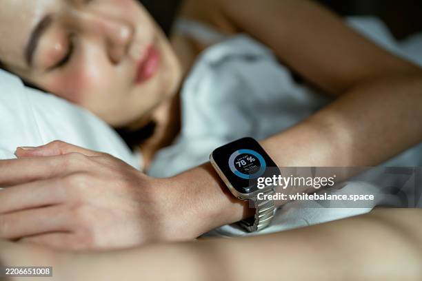 woman sleeping peacefully in bed, wearing a smart watch to track her sleep - wearable stock-fotos und bilder