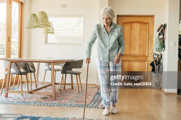 senior woman practicing mobility in a cozy home setting, using a walking stick for support and stability. - walking cane stock pictures, royalty-free photos & images