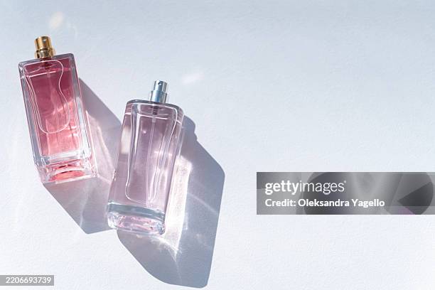 two elegant perfume bottles casting soft shadows on a light surface, showcasing their unique designs and colors - perfume fotografías e imágenes de stock