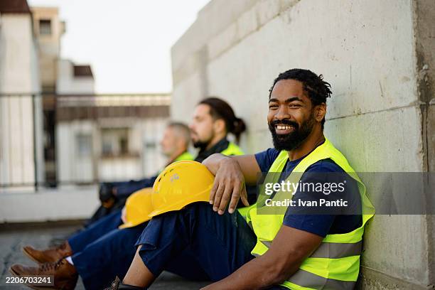 construction workers in safety vests resting and smiling at job site - reflective clothing stock pictures, royalty-free photos & images
