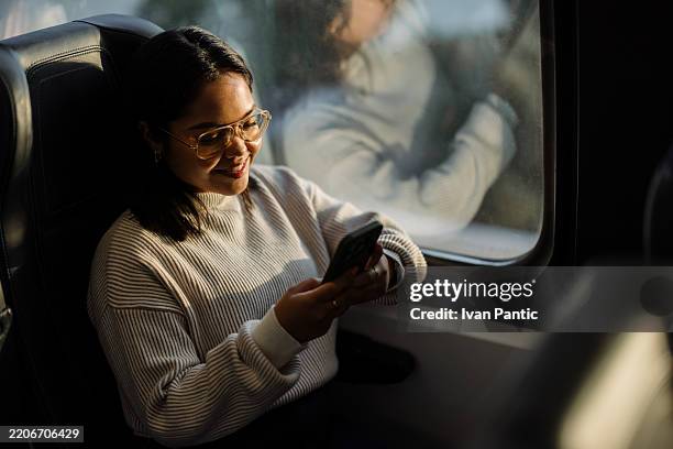 woman using smartphone while traveling, smiling and relaxing on public transportation - rail transportation stock pictures, royalty-free photos & images