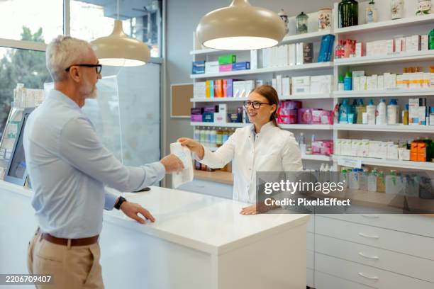 smiling female pharmacist giving medication in a paper bag to a customer - apotheek stockfoto's en -beelden