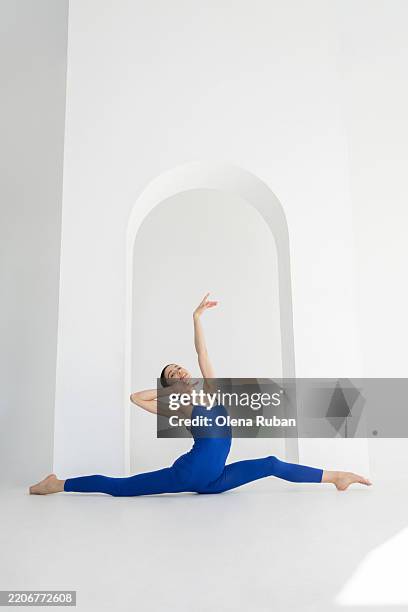 cheerful young woman in a blue leotard doing twine in a white studio. - acrobatic activity stock pictures, royalty-free photos & images