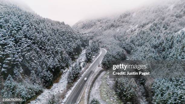 an aerial/drone view of a delivery van on a road through the snow covered forest in the spanish pyrenees mountains - pirineos fotografías e imágenes de stock