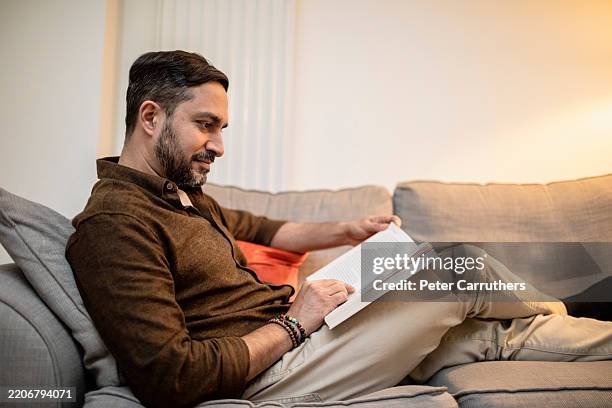 profile view of a man sitting on a sofa reading a book - asian man side profile stock pictures, royalty-free photos & images