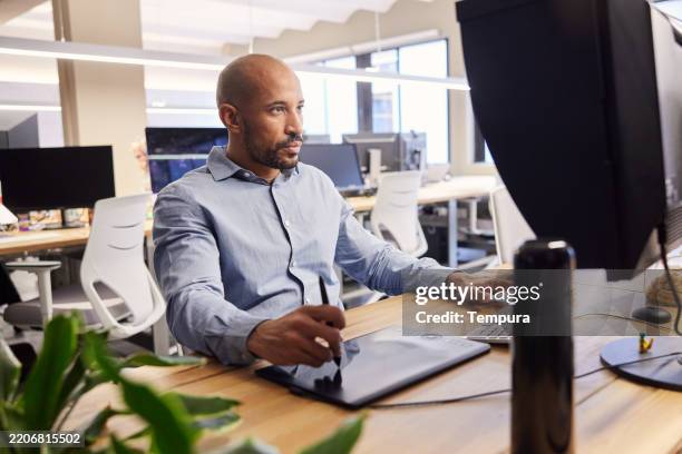 un hombre trabajando en una computadora de escritorio usando un bolígrafo digital. - profesional de diseño fotografías e imágenes de stock