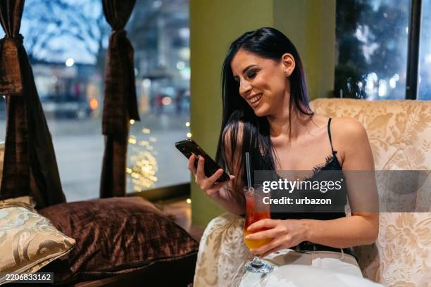 young woman using a phone while drinking a cocktail in a bar at night - tonic water stock pictures, royalty-free photos & images