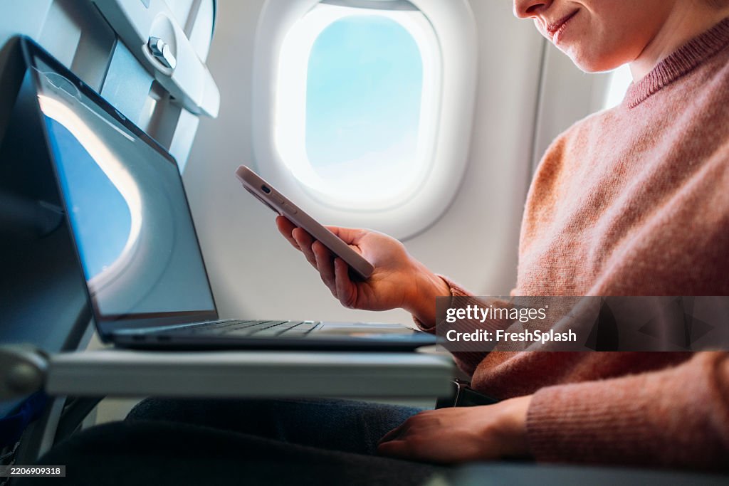 飛行機のフライトでスマートフォンとラップトップを使用するビジネストラベラー