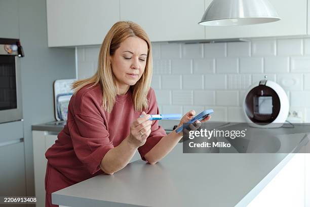 mujer usando un teléfono inteligente mientras sostiene una pluma de insulina - insulina fotografías e imágenes de stock