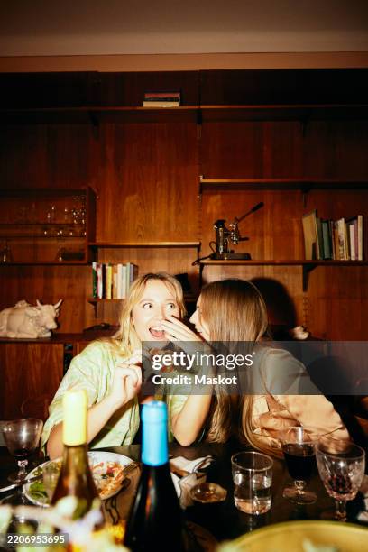 young female friends gossiping with each other while sitting at dining table - fluisteren stockfoto's en -beelden