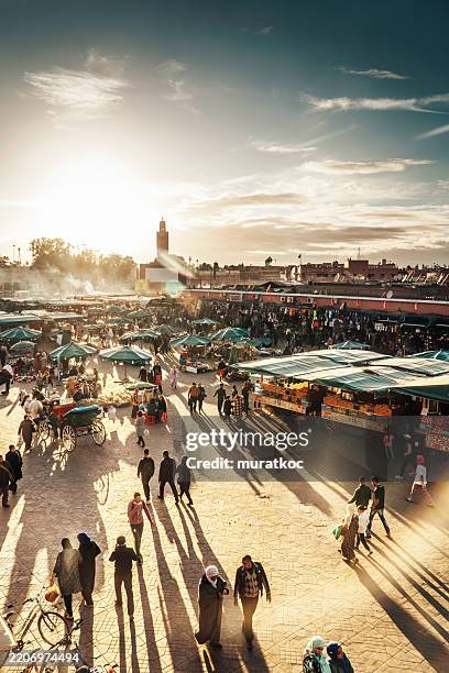 marrakeschs berühmter djemaa el fna-platz bei sonnenuntergang mit der koutoubia-moschee im hintergrund - marktplatz stock-fotos und bilder