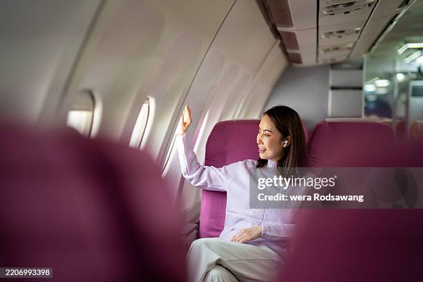 female passenger enjoys breathtaking scenery from airplane window while listening to music through in-ear headphones - flugzeugsitz stock-fotos und bilder