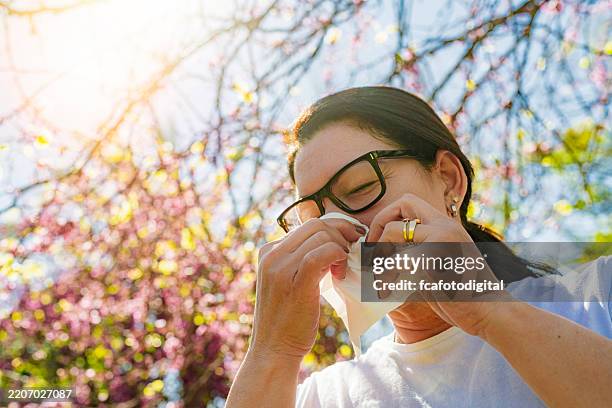 reife frau mit saisonaler allergie, die sich mit papiertaschentuch die nase putzt - sinusitis stock-fotos und bilder