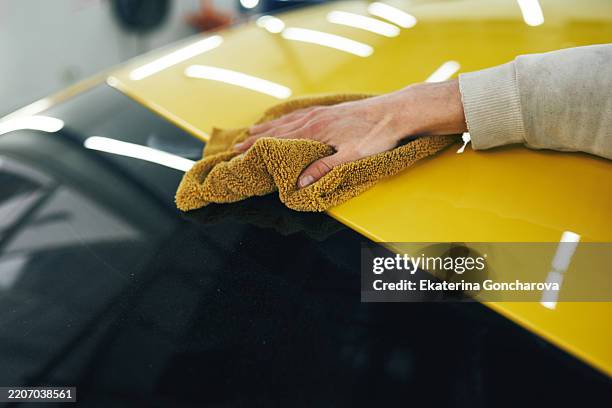 hand cleaning a yellow vehicle surface with microfiber cloth in workshop - mikrofaser stock-fotos und bilder