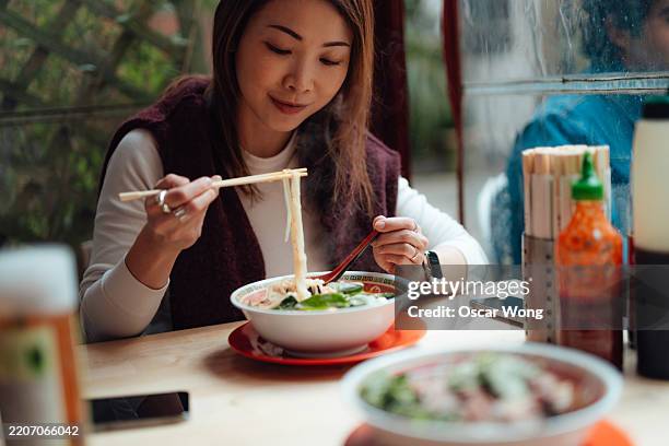young asian woman eating vietnamese pho at a local restaurant - spring onion soup stock pictures, royalty-free photos & images