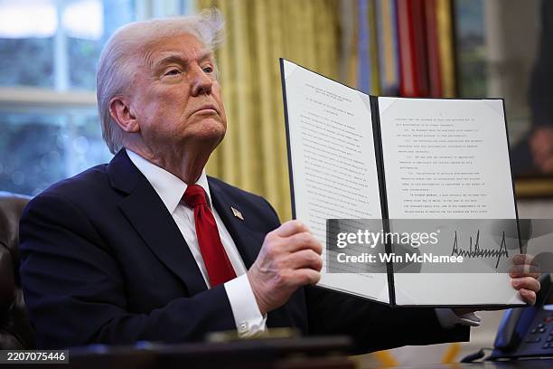 President Donald Trump displays a signed an executive order in the Oval Office of the White House on March 26, 2025 in Washington, DC. President...