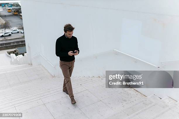 businessman walking downstairs while using smartphone - people looking down stock pictures, royalty-free photos & images