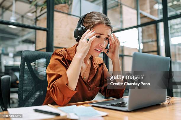 customer support officer at desk, pressing temples, looking worried at laptop in call center - een dag uit het leven serie stockfoto's en -beelden